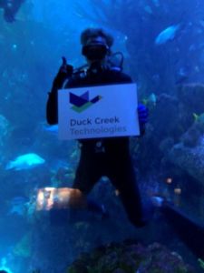 a diver at the new england aquarium holds a duck creek technologies sign